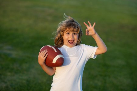 Téléchargez les photos : Football américain. Un gamin jouant avec une balle de rugby dans le parc. Portrait d'un garçon tenant un ballon de football américain dans un parc. - en image libre de droit