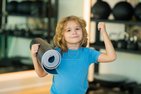 Photo for Cute kid showing biceps holding yoga mat in gym. Yoga child concept. Young strong sporty kid showing biceps. Workout sport concept - Royalty Free Image