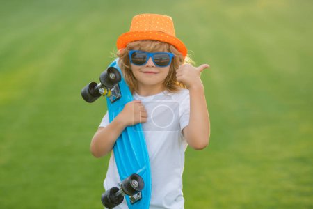Téléchargez les photos : Child boy holding longboard on pink background. Kid with pennyboard. Outdoor portrait of cheerful little kid with penny board. Summer kids fashion - en image libre de droit
