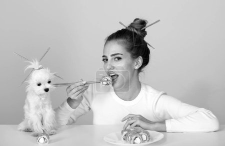 Photo for Sexy woman eat japanese traditional food sushi rolls. Girl is holding japanese sushi piece of roll philadelphia by chopsticks. Advert for sushi delivery of restaurants cafe. Advertising with dog pet - Royalty Free Image