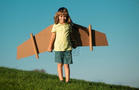 Téléchargez les photos : Portrait d'enfant blond mignon jouer pilote avec des ailes d'avion en papier artisanal fait main. Enfants rêvant, succès, concept créatif et start-up - en image libre de droit