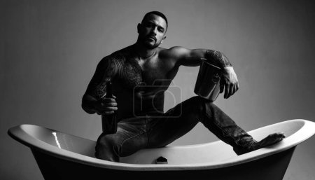 Photo for The best way to relax after a stressful workday. Atheltic hispanic man drinking champagne to relax. Strong latino man with tattoo on fit torso relax and enjoy in bath. Stress relieving spa relax. - Royalty Free Image