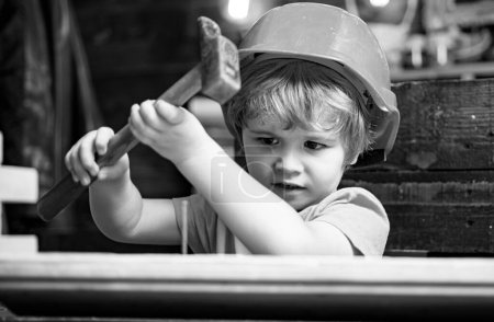 Foto de Niño en sombrero duro sosteniendo tablón de madera y martillo. Ingeniero infantil con martillo de carpintería sobre madera - Imagen libre de derechos