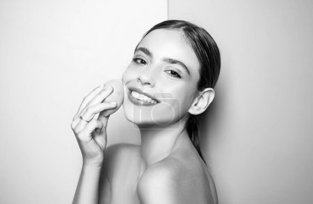 Photo for Healthy smiling girl with bare shoulders, clear skin, dark hair and beige sponge. Natural makeup look. Health and beauty concept. Happy young woman covering her skin with foundation - Royalty Free Image