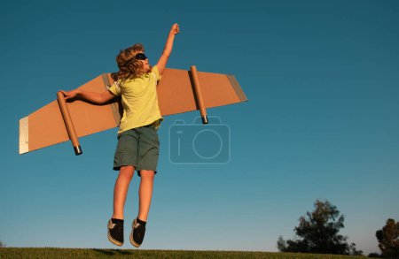 Téléchargez les photos : Enfant super héros sauter et voler avec jetpack. Enfant pilote jouer le jour d'été. Succès, concept de leader et gagnant. Imagination et liberté - en image libre de droit