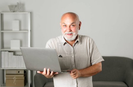 Téléchargez les photos : Grand-père, portrait d'un homme âgé avec un ordinateur portable. Homme âgé avec une barbe grise à la maison. Homme mûr utilisant un ordinateur - en image libre de droit