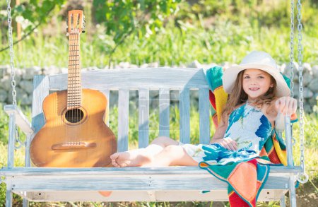 Foto de Fashion child in summer straw hat swing in the summer park. Summer holidays with children. Child chill and resting in summer holiday - Imagen libre de derechos