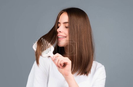 Photo for Beautiful woman combs her healthy hair. Combing healthy long straight female hair, close up. Attractive gorgeous cheerful positive girl combing shine silky hair, isolated - Royalty Free Image