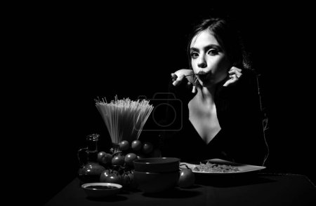 Hungrige schöne Frau essen auf Nudeln Spaghetti auf schwarzem Hintergrund