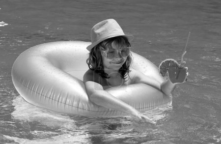 Téléchargez les photos : Cocktail dans la piscine. L'enfant se repose dans la piscine avec une boisson aux fruits. Vacances d'été - en image libre de droit