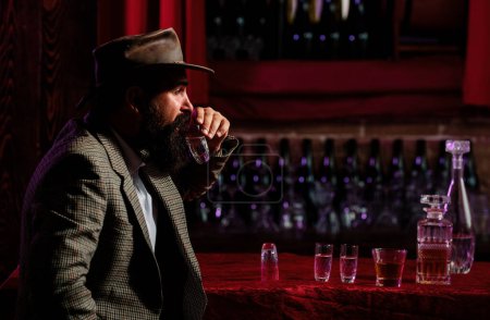 Foto de Trabajador vintage con barba larga sosteniendo whisky. Sentado en el bar - Imagen libre de derechos