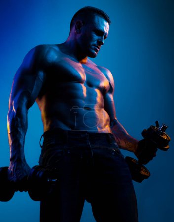 Foto de Muscular culturista chico haciendo ejercicios con pesas aisladas en neón azul. Atleta desnudo con cuerpo fuerte. Sin camisa con abdominales perfectos - Imagen libre de derechos