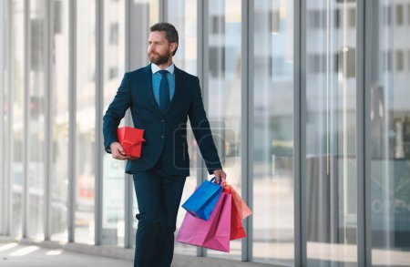 Téléchargez les photos : Homme d'affaires faisant du shopping en ville. bel homme en costume avec des sacs à provisions - en image libre de droit