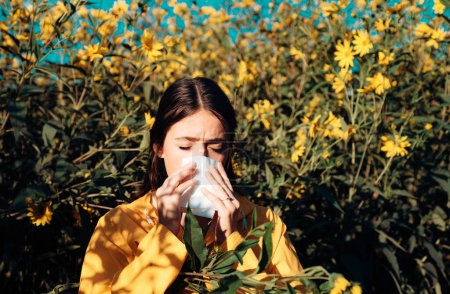 Foto de Concepto de alergia al polen. La joven va a estornudar. Primer plano retrato de niña estornudando en el fondo de flores amarillas. Hermosa chica que tiene una reacción alérgica a las flores - Imagen libre de derechos