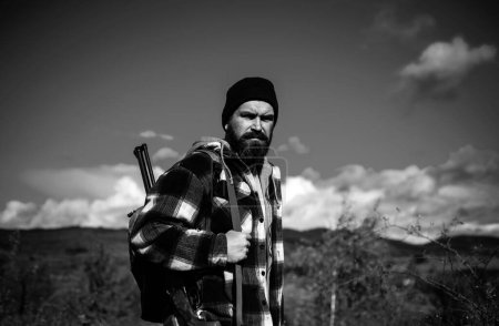 Hunter con escopeta a la caza. Hombre cazador barbudo sosteniendo arma y caminando en el bosque. Otoño
