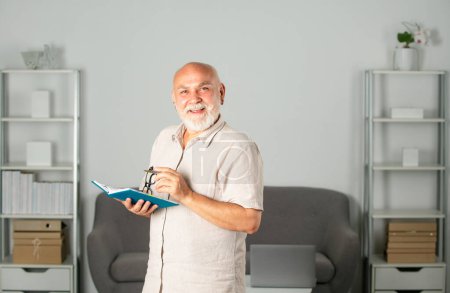 Consultor maduro, nota de hombre mayor con bolígrafo en libro de texto en la oficina. Hombre de negocios senior escribiendo en cuaderno