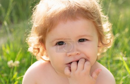 Foto de Bebé niño en la hierba en el fieald en verano. Cara de bebé de cerca. Gracioso retrato de primer plano de niño. Niño rubio, cara de emoción - Imagen libre de derechos