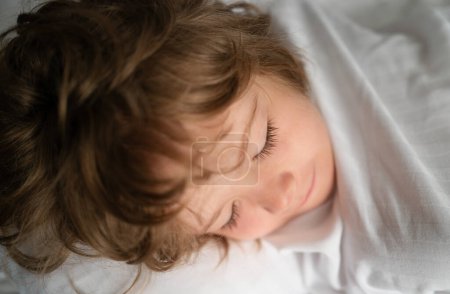 Téléchargez les photos : Enfants dormant seuls dans un lit confortable avec des draps blancs - en image libre de droit