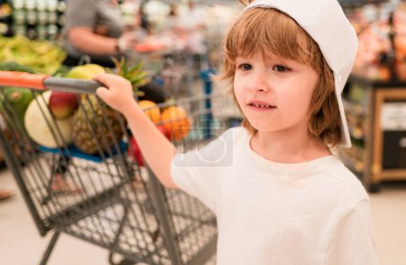 Photo for Sale, consumerism and people concept - happy little child with food in shopping cart at grocery store - Royalty Free Image