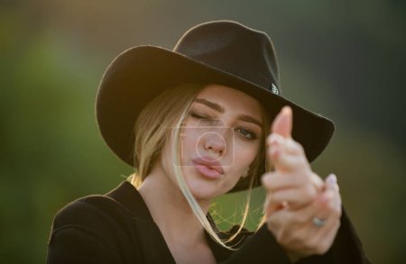 Photo for Beautiful woman in fashion hat. Portrait of a young woman, close up face of beautiful woman outdoor. Cheerful female model. Cowgirl shooting with finger gun - Royalty Free Image