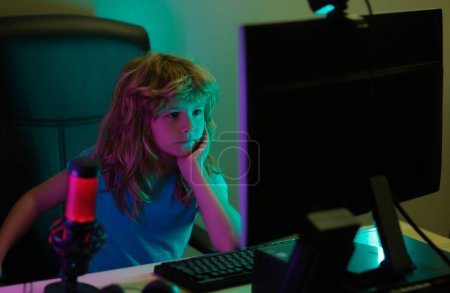 Clever kids learning online home. Caucasian child boy working on laptop in dark room at night. Social network for kids