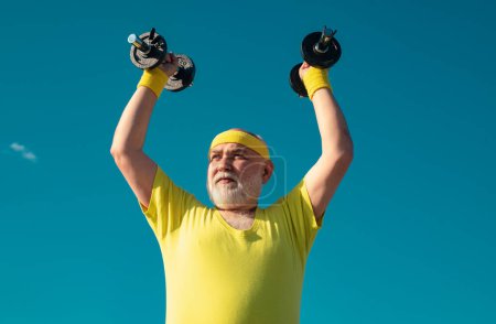 Senior man in health club. Old mature man exercising with dumbbell. Portrait of senior man holding dumbbell. Senior male is enjoying sporty lifestyle