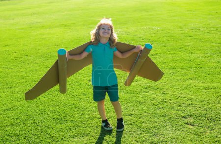 Niño feliz con alas de papel contra hierba verde. Niño con juguete jetpack divertirse en primavera campo verde al aire libre. Libertad despreocupado y niños imaginación sueño concepto