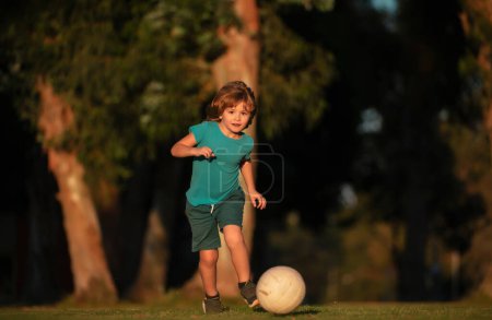 Téléchargez les photos : Enfant garçon jouant au football sur le terrain de football. Un gamin qui joue au foot. Enfant footballeur dans le parc - en image libre de droit