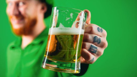 Portrait of excited man holding glass of beer on St Patricks day isolated on green