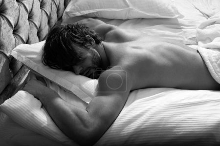 Handsome man sleeping on bed in bedroom. Waist up portrait of muscular handsome guy laying on stomach in bed and having nap embracing the pillow