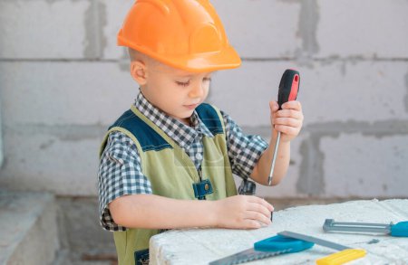 Téléchargez les photos : Little boy holding screwdriver. Kid twists bolt with screwdriver. Little Repairman with repair tool. Cute kid as a construction worker. Childrens play with a hammer pliers and screwdriver - en image libre de droit