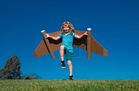 Glückliches Kind, das mit Papierflügeln gegen den blauen Himmel springt. Porträt eines Jungen, der mit einem Spielzeug-Jetpack spielt. Freiheit sorgenfrei, Erfolgssieger, Innovations- und Vorstellungskonzept