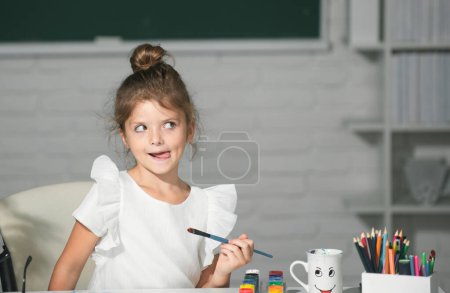 Foto de Divertido niño niña pintura con pinturas de color y pincel. Lección de dibujo en la escuela. Aprendizaje infantil, habilidades artísticas para niños - Imagen libre de derechos