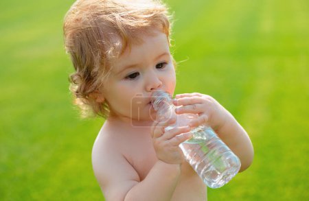 Photo for Child drinks water from a bottle while walking on grass field, baby health. Baby drinking water - Royalty Free Image