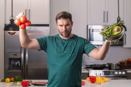 Téléchargez les photos : Homme dans la cuisine moderne, préparant des aliments sains seul, cuisine salade. Beau homme prépare une salade végétalienne fraîche dans la cuisine à la maison. Une alimentation saine est une vie saine - en image libre de droit