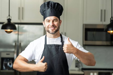 Téléchargez les photos : Joyeux chef cuisinier avec le pouce levé. Homme en chef chapeau cuisine sur la cuisine - en image libre de droit