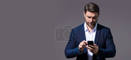Photo for Portrait of handsome man in suit using smartphone, chatting, making post on social media. Business man call on phone isolated over studio background. Banner for header, copy space - Royalty Free Image