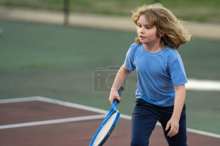 Téléchargez les photos : Il joue au tennis sur le terrain. Enfant frappé balle de tennis avec raquette de tennis. Exercice actif pour les enfants. Activités estivales pour les enfants. Enfant apprenant à jouer au tennis. Le gamin frappe la balle sur le terrain - en image libre de droit