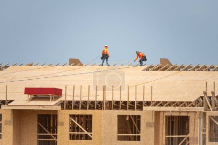 Photo for Roof construction. Roofer on roof structure. Construction Worker on Top of the Wooden House Frame. Worker roofer builder working on roof at construction site. Construction crew working on the roof - Royalty Free Image