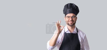 Téléchargez les photos : Beau cuisinier ou boulanger homme en tablier, chemise et chapeau de cuisine isolé sur fond gris. Cuisine concept de nourriture. Maquette de l'espace de copie. Chef Man en chapeau de chef. Bannière isolée de cuisson homme - en image libre de droit