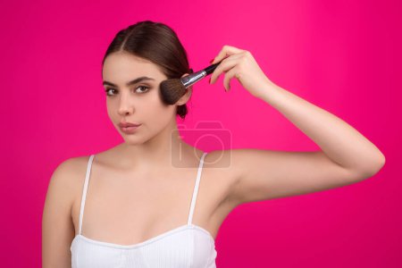 Mujer joven que aplica polvo base o rubor con cepillo de maquillaje. Tratamiento facial, piel perfecta, maquillaje natural, belleza facial. Aislado en el fondo del estudio. Aplicar maquillaje