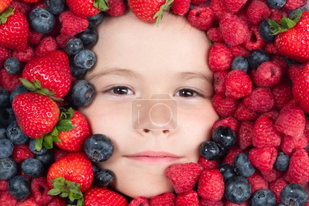 Téléchargez les photos : Des fruits drôles. Les baies mélangent myrtille, framboise, fraise, mûre. Visage enfant avec cadre Berry, gros plan - en image libre de droit