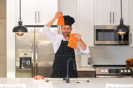 Téléchargez les photos : Un homme hispanique millénaire en uniforme de chef tient du saumon de poisson à la cuisine. Cuisiner du poisson. Menu restaurant avec poisson saumon. Cuisine, publicité saumon poisson concept - en image libre de droit