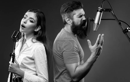 Photo for Singer duet couple is performing a song with a microphone while recording in a music studio - Royalty Free Image