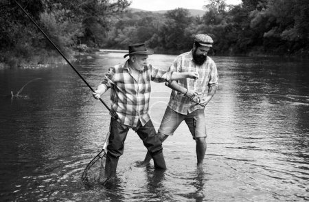 Téléchargez les photos : Father and mature son fisherman fishing with a fishing rod on river. Happy excited man friends - en image libre de droit