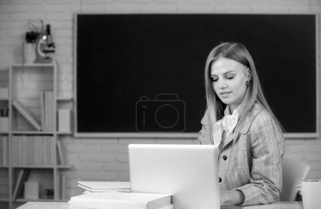 Photo for Female student sitting at table and writing on notebook in classroom at high school or college - Royalty Free Image