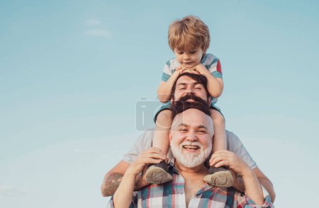 Téléchargez les photos : Joyeuse fête des pères. Père et fils profitent du plein air. génération hommes : grand-père père père et petit-fils sont câlins regardant caméra et souriant - en image libre de droit