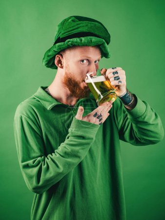Lucky charms on green background. Leprechauns hat. Man on green background celebrate St Patricks Day. Portrait of excited man holding glass of beer on St Patricks day isolated on green