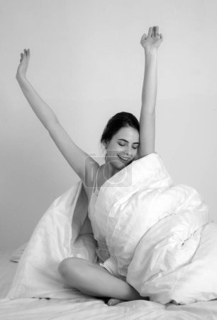 Photo for Woman stretching in bed after waking up, happy and relaxed after good sleep. Sweet dreams, good morning, new day. She keeps eyes closed and looks sexy - Royalty Free Image
