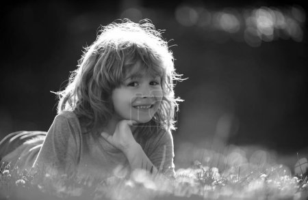 Téléchargez les photos : Portrait d'un enfant heureux riant allongé sur l'herbe dans le parc naturel d'été. Gros plan positif enfants visage - en image libre de droit
